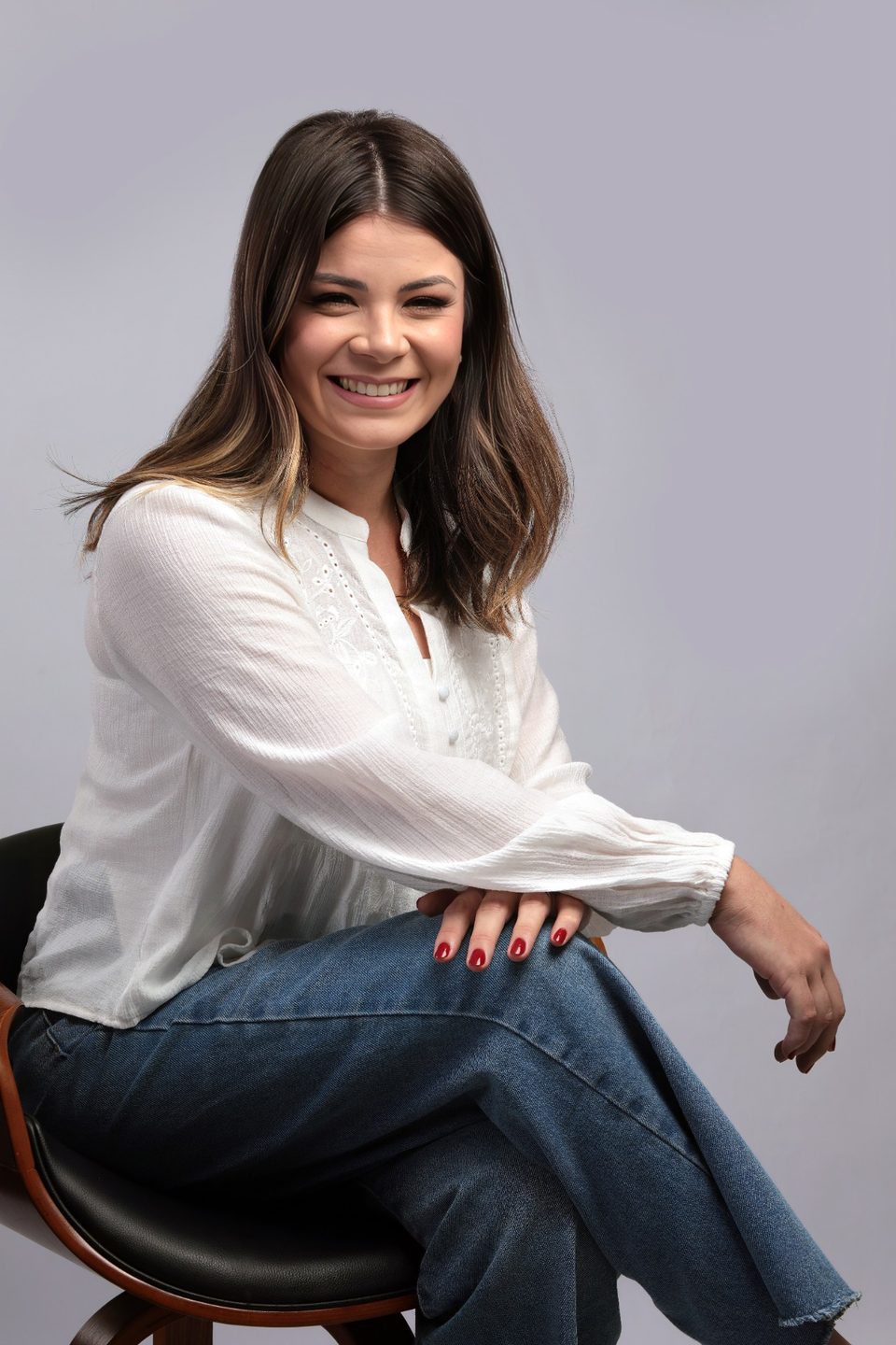 Samara Gregório sorrindo, sentada num banquinho, de blusa branca