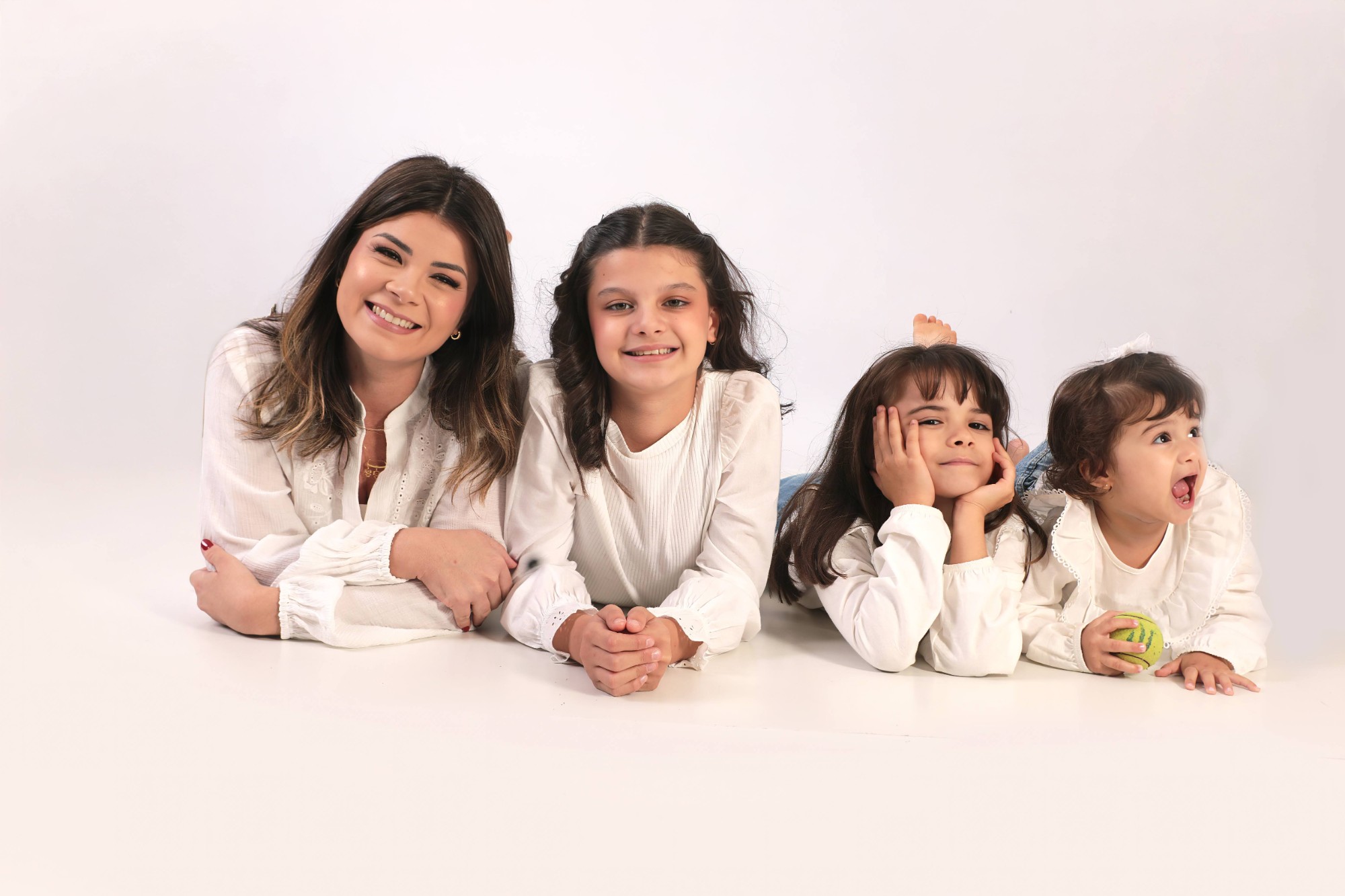 Samara deitada no chão com as três filhas, todas de branco, rindo